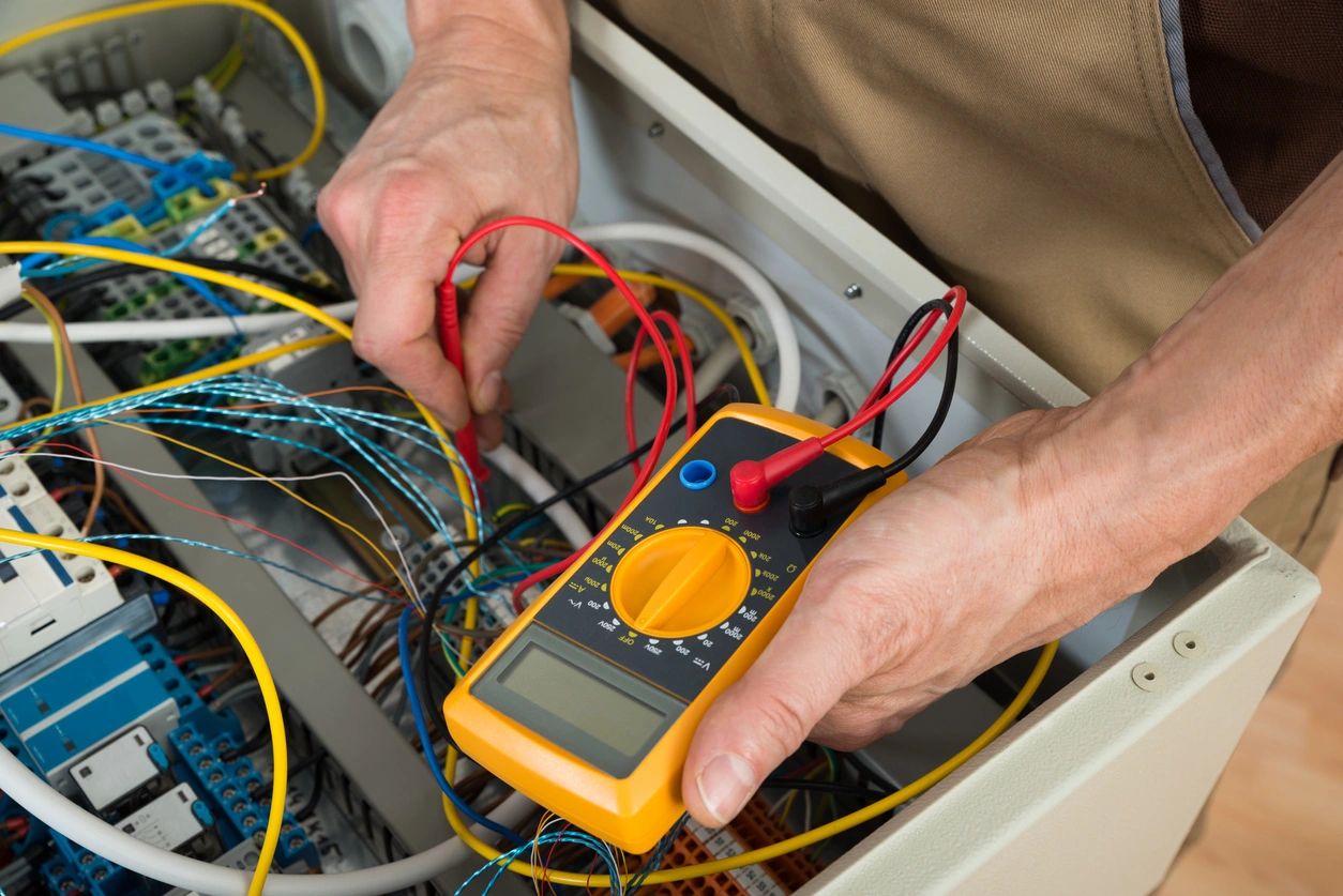 Hands testing wiring in a panel with a multimeter