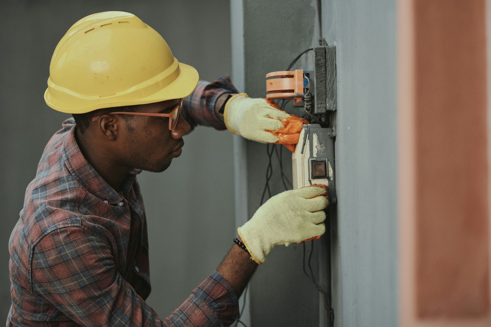 Electrician in a hard hat working on a wall electrical panel
