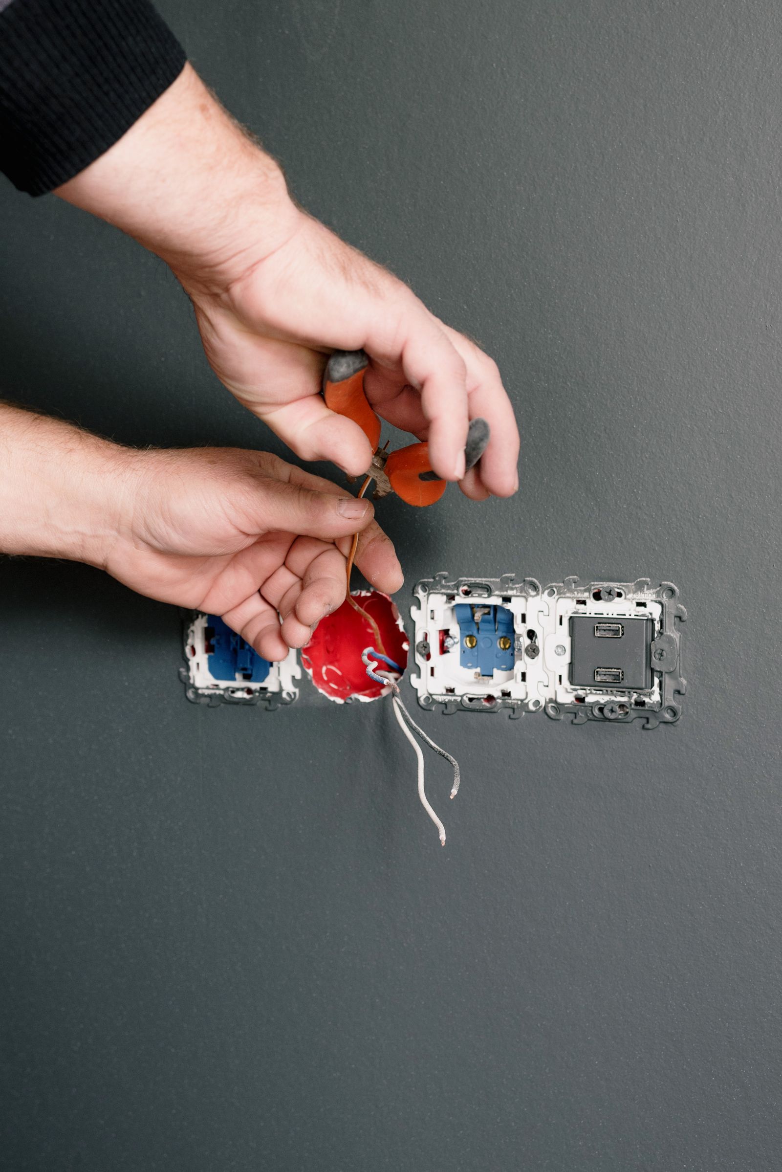 Hands installing new sockets on a gray wall